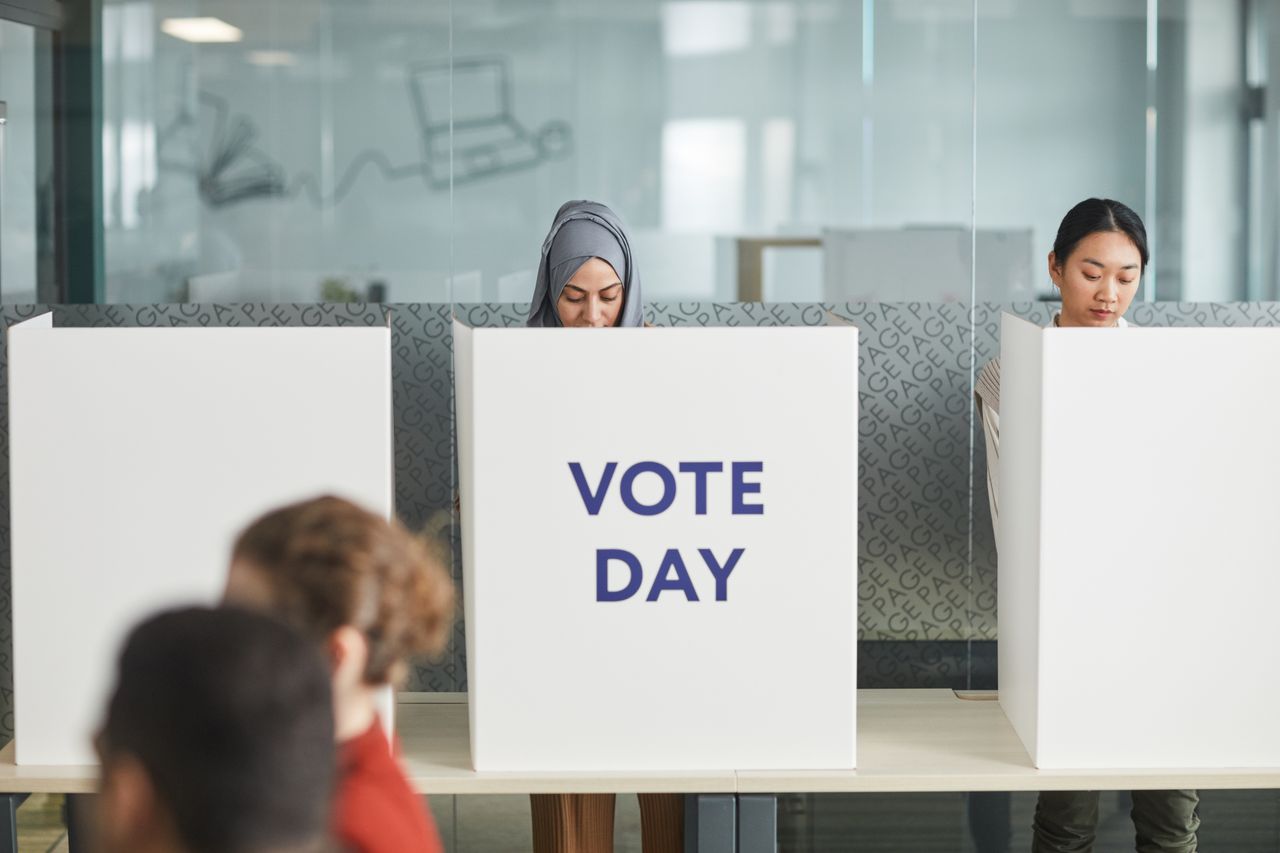 brand-01 Two women casting their votes in an office during election day, focusing on diversity and civic engagement.