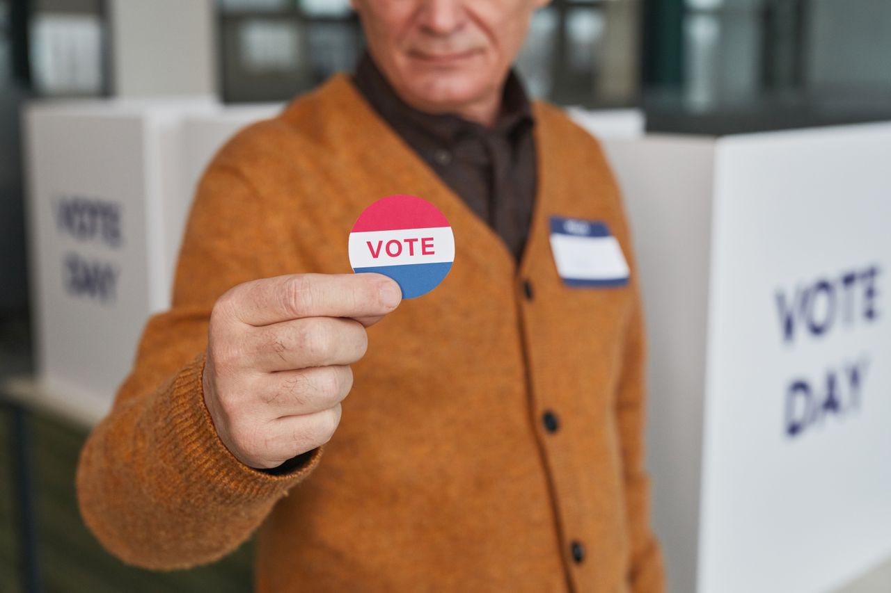 creative-02 A senior adult holding a vote sticker inside a polling booth during election day.