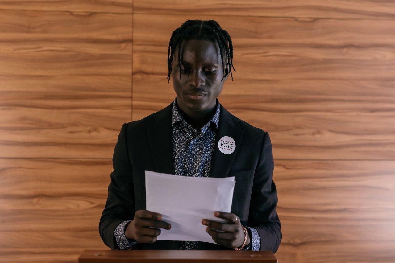 creative-03 Black man wearing a suit addressing a document, possibly in a political setting.